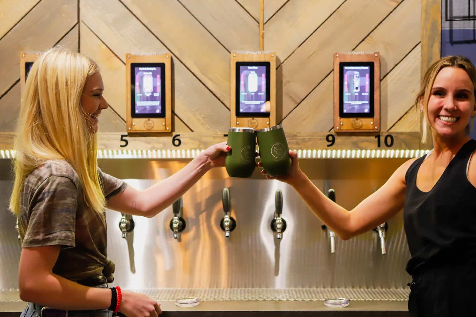 two women at Oakwell Beer Spa in Denver serving themselves with beer from the self-serve beer wall
