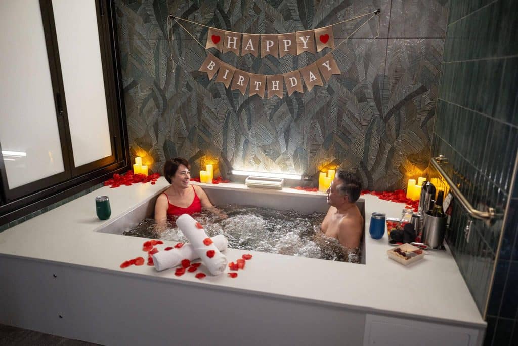 Couple in a beer bath with candles, rose petals, and a Happy Birthday banner at Oakwell Beer Spa