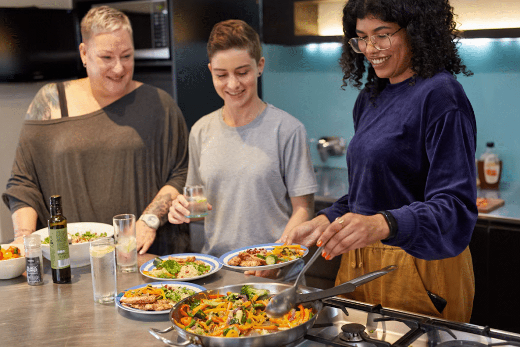 Three people smile as they sample food made during their cooking class