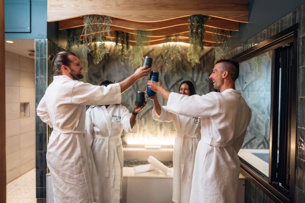Four people in robes hold a toast with their beers inside a private beer bath suite.