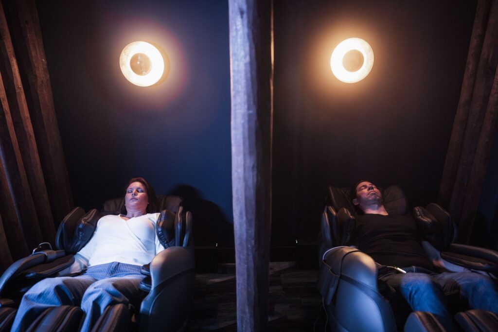 A couple relaxes side-by-side in the Relaxation Lounge zero-gravity massage chairs