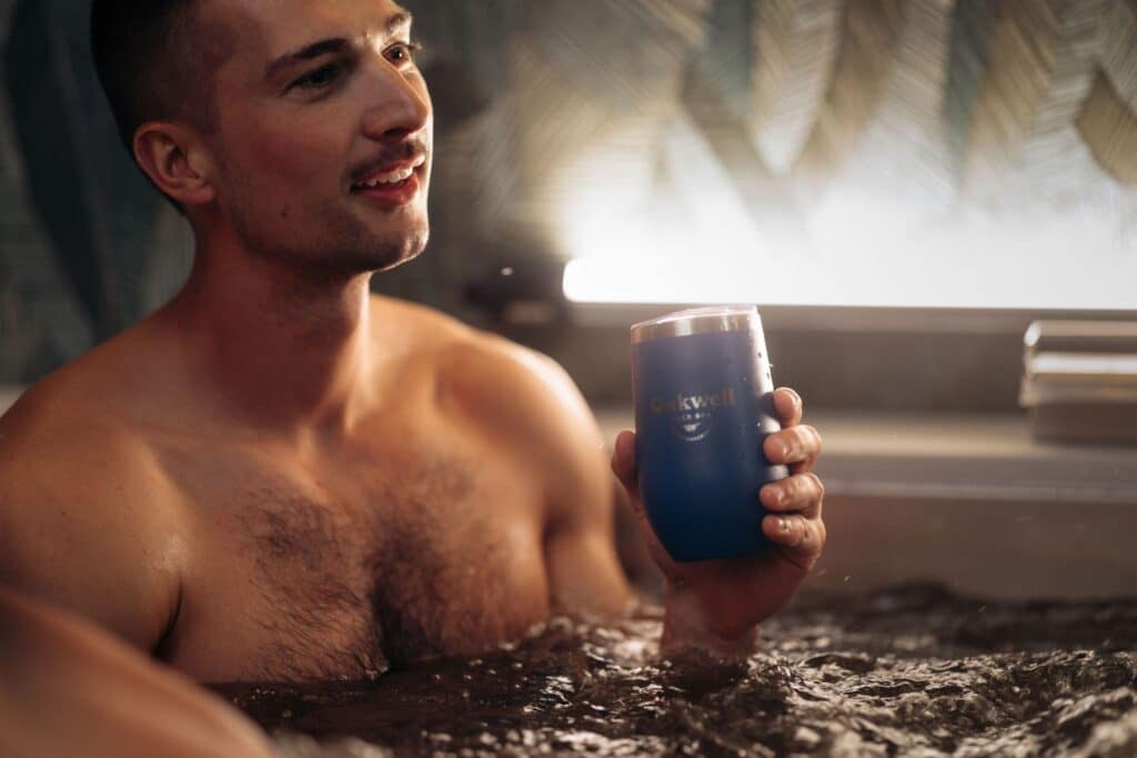 A man sips on a craft beverage while soaking in a private Oakwell spa suite