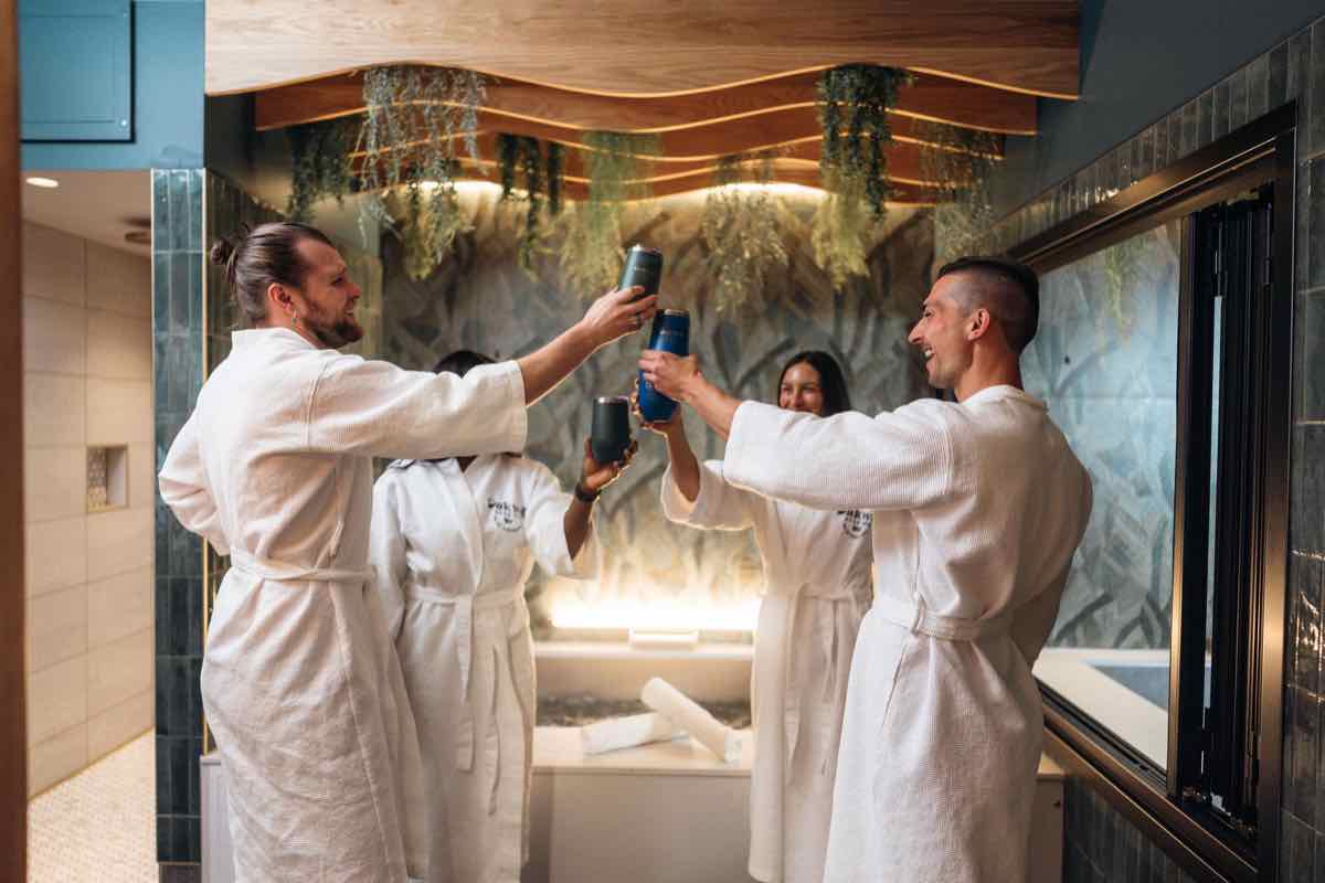 Four people in robes hold a toast with their beers inside a private beer bath suite